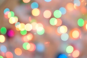 Verschwommene, bunte Lichtpunkte in Gelb, Grün, Blau und Orange erzeugen einen sanften Bokeh-Effekt auf einem hellen Hintergrund.