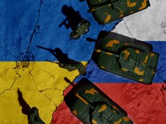 Eine Draufsicht auf Spielzeugsoldaten und Panzer, die auf einem rissigen Untergrund platziert sind, der die Nationalflaggen der Ukraine und Russlands zeigt und so den militärischen Konflikt symbolisiert.