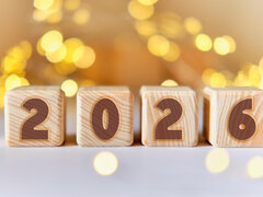 Vier Holzklötze mit der Zahl 2026 vor warmen, goldenen Lichtern.